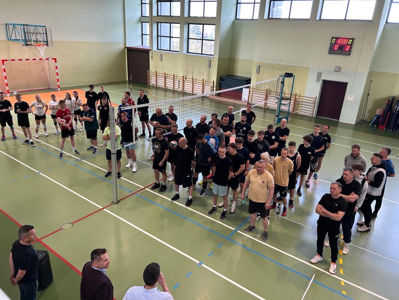 Drużyny stojące w sali gimnastycznej. Rozdziela ich siatka. Przygotowaania do rozgrywek 