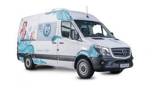 Dentobus - samochód z mobilnym punktem stomatologicznym. Biały samochód oklejony reklamami. 