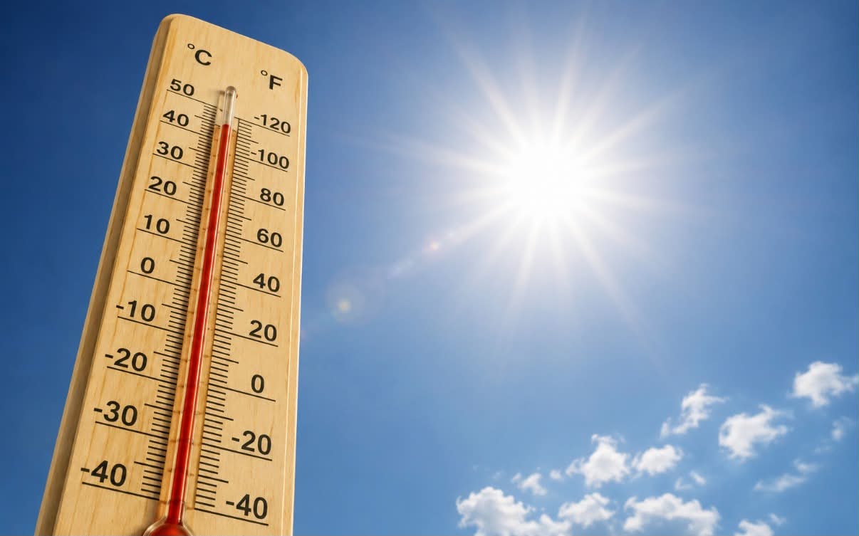 Termometr pokazujący wysoką temperaturę, bezchmurne niebo i słońce. 