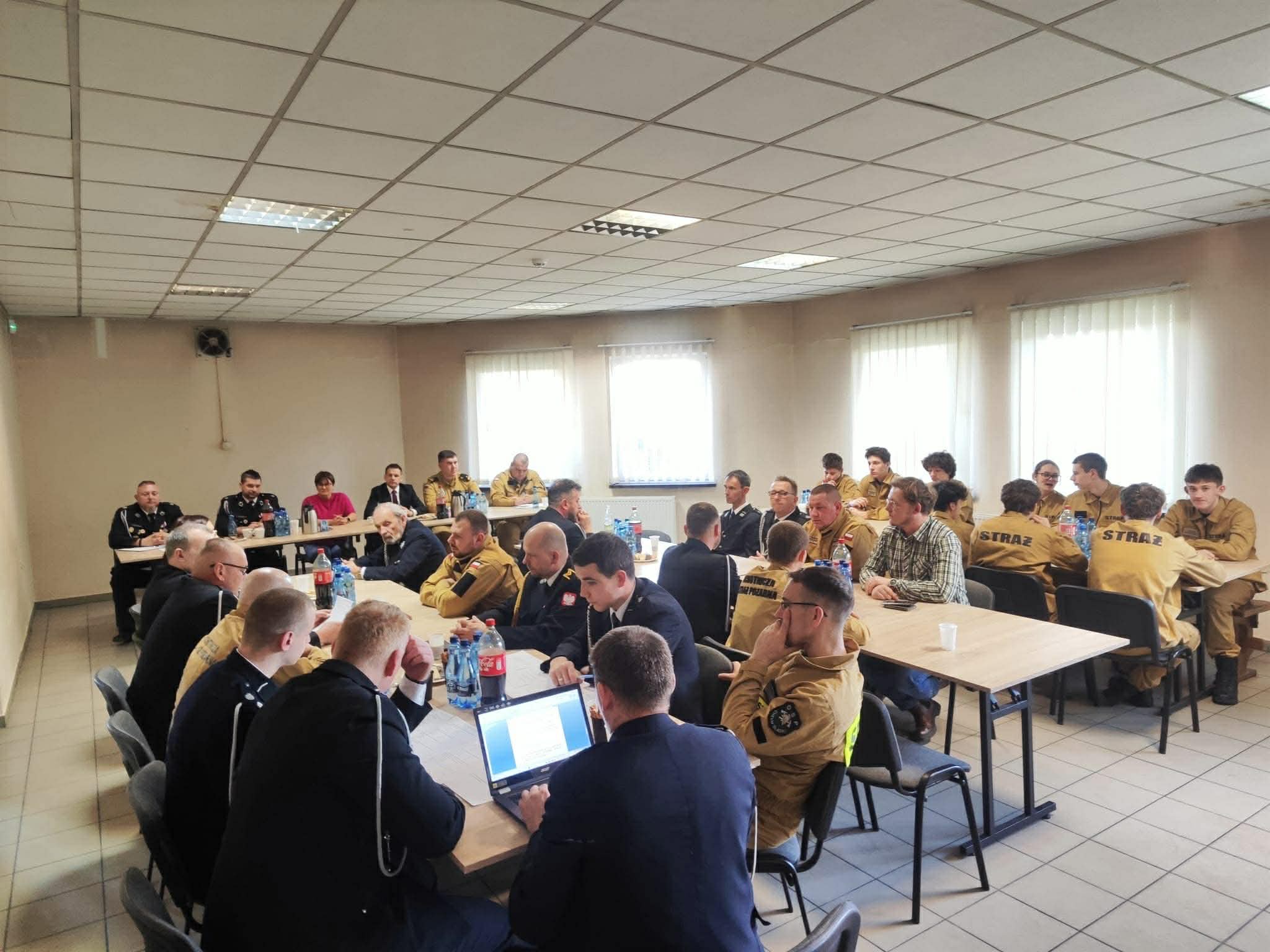 W pomieszczeniu siedzący za stołami druhowie i zaproszeni goście podczas spotkania 