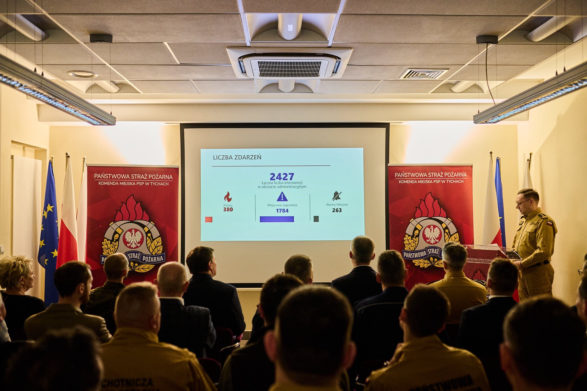 Pomieszczenie a w nim siedzące osoby w układzie konferencyjnym uczestniczące w pokazie prezentacji