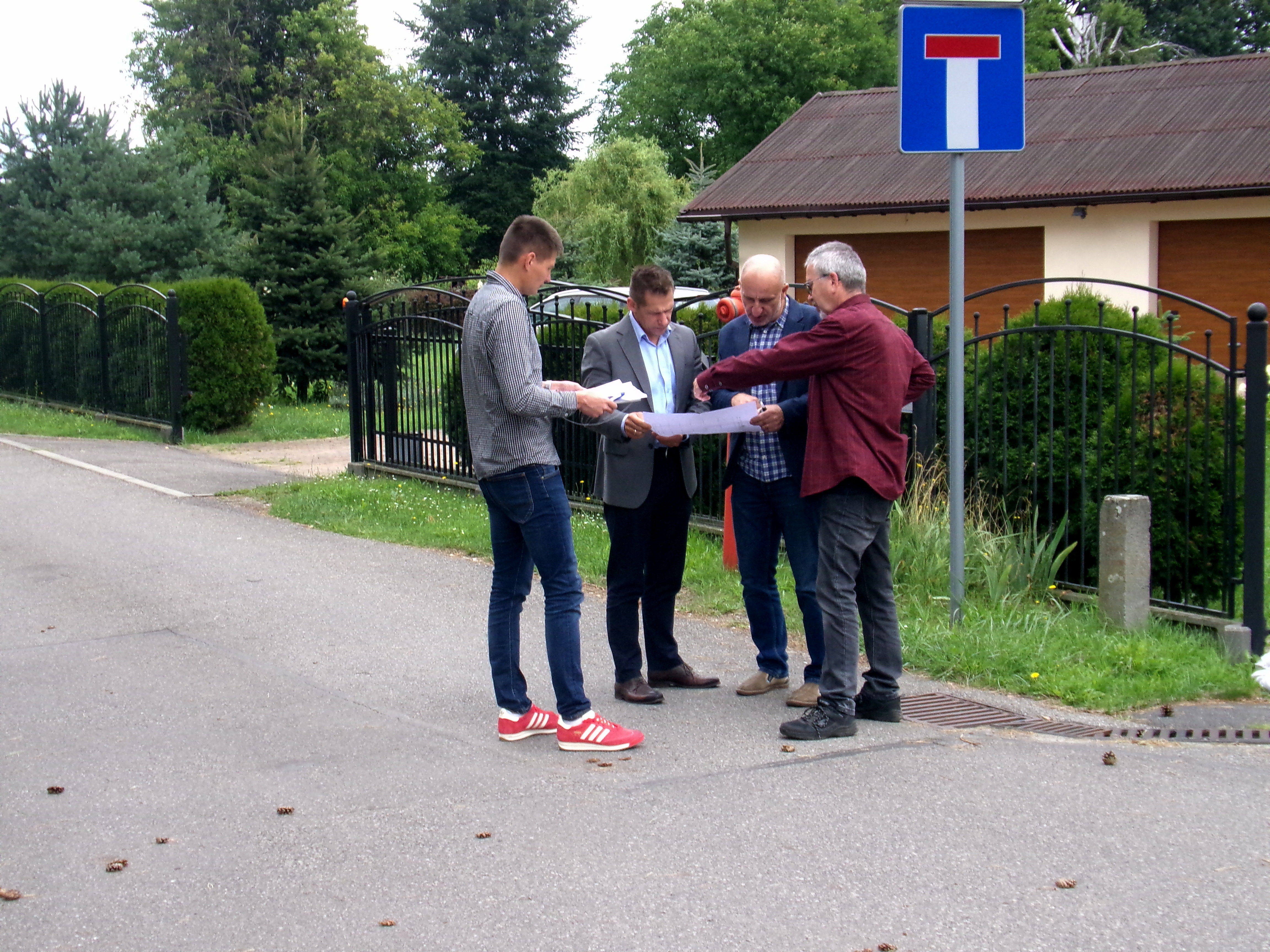 Czterej mężczyźni stojący na drodze. W tle zabudowania