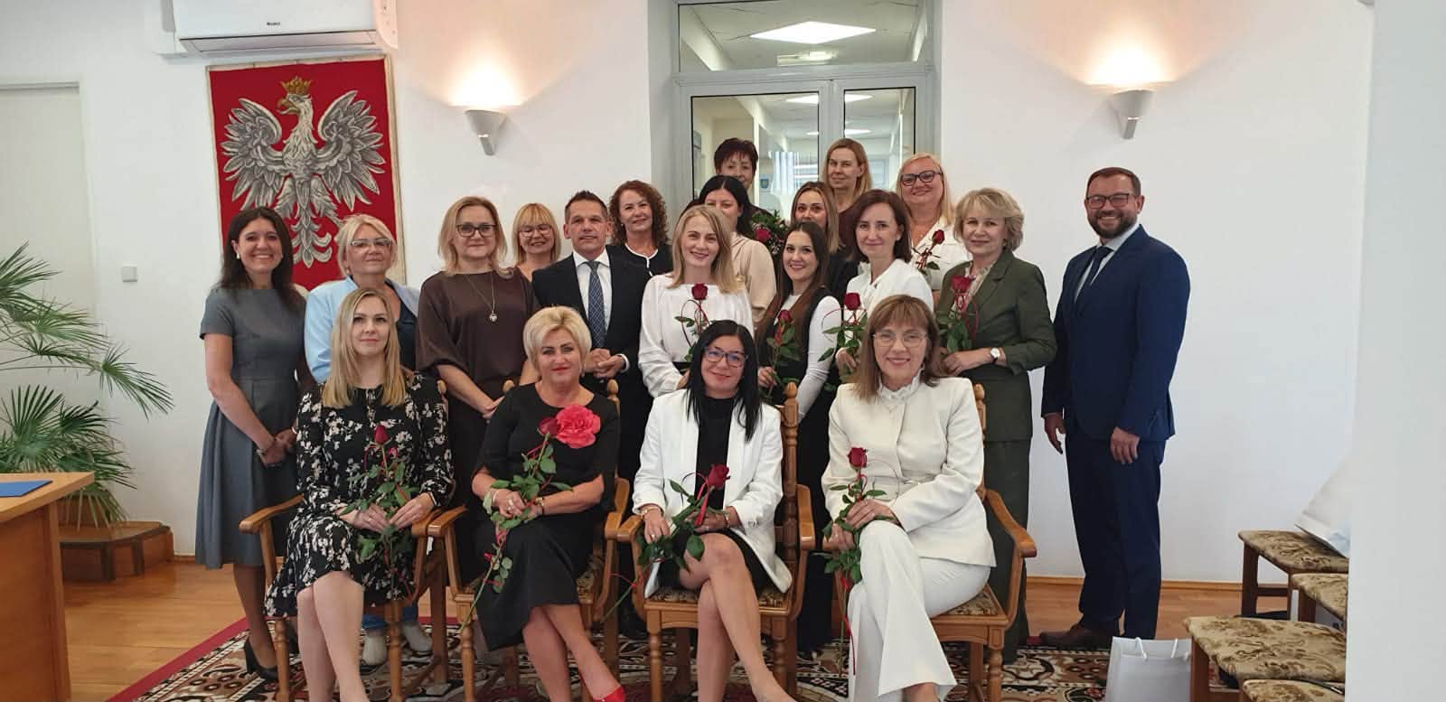 Kobiety i mężczyźni pozujący do zdjęcia w pomieszczeniu. Częśc z nich siedzi 