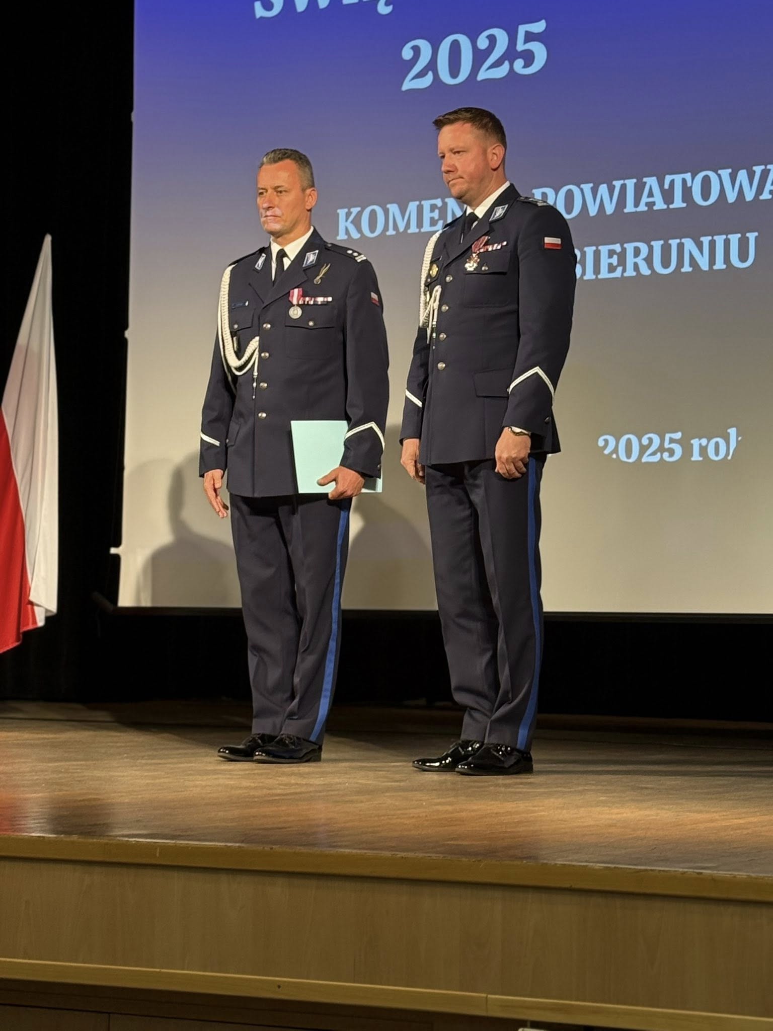 Dwóch mężczyzn w mundurach policyjnych stojących na scenie. 