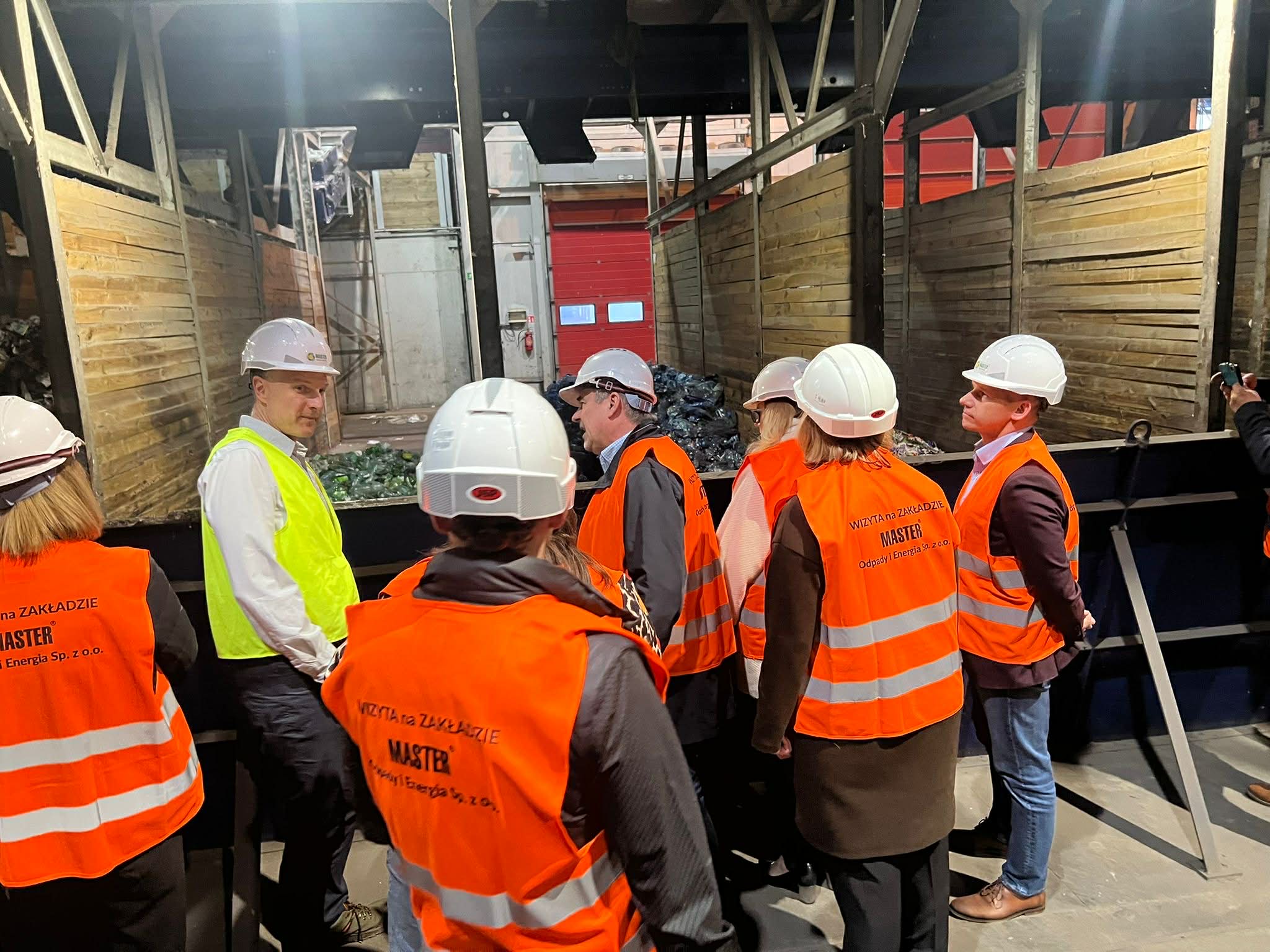 Osoby stojące w pomieszczeniu w kamizelkach odblaskowych i kaskach 