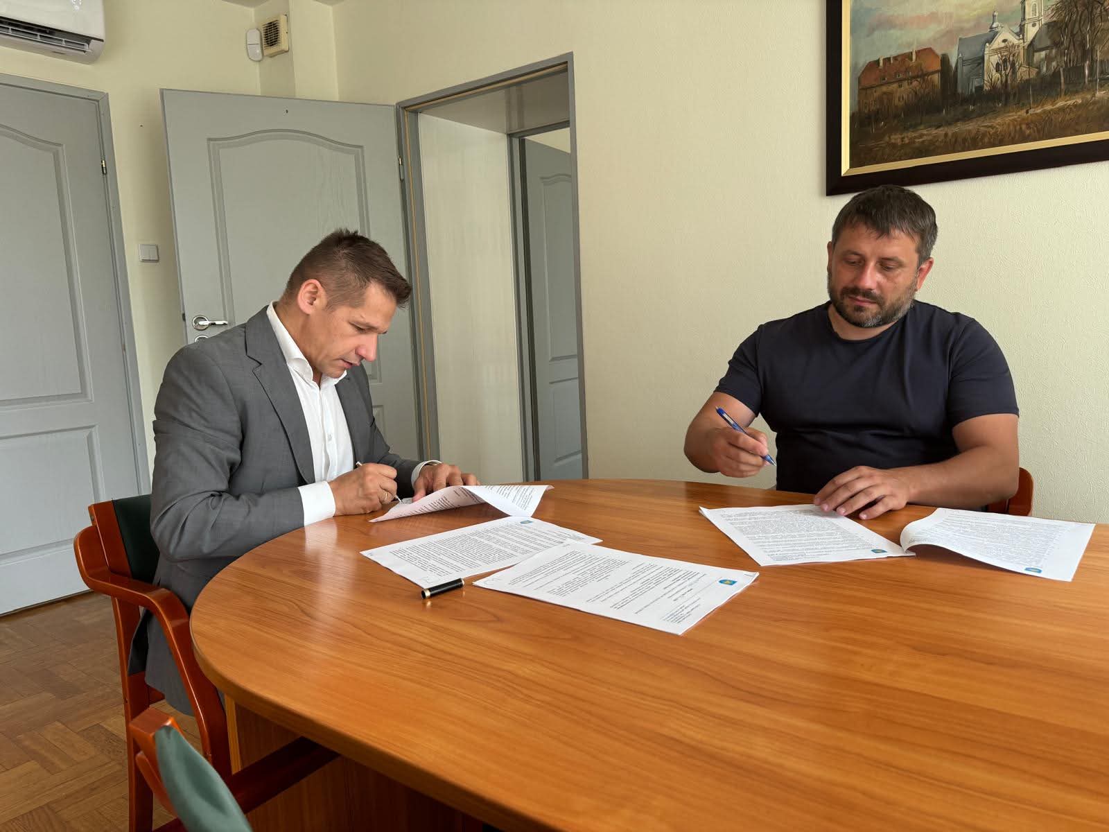 Dwaj mężczyźni w pomieszczeniu przy stole podpisują dokumentację 