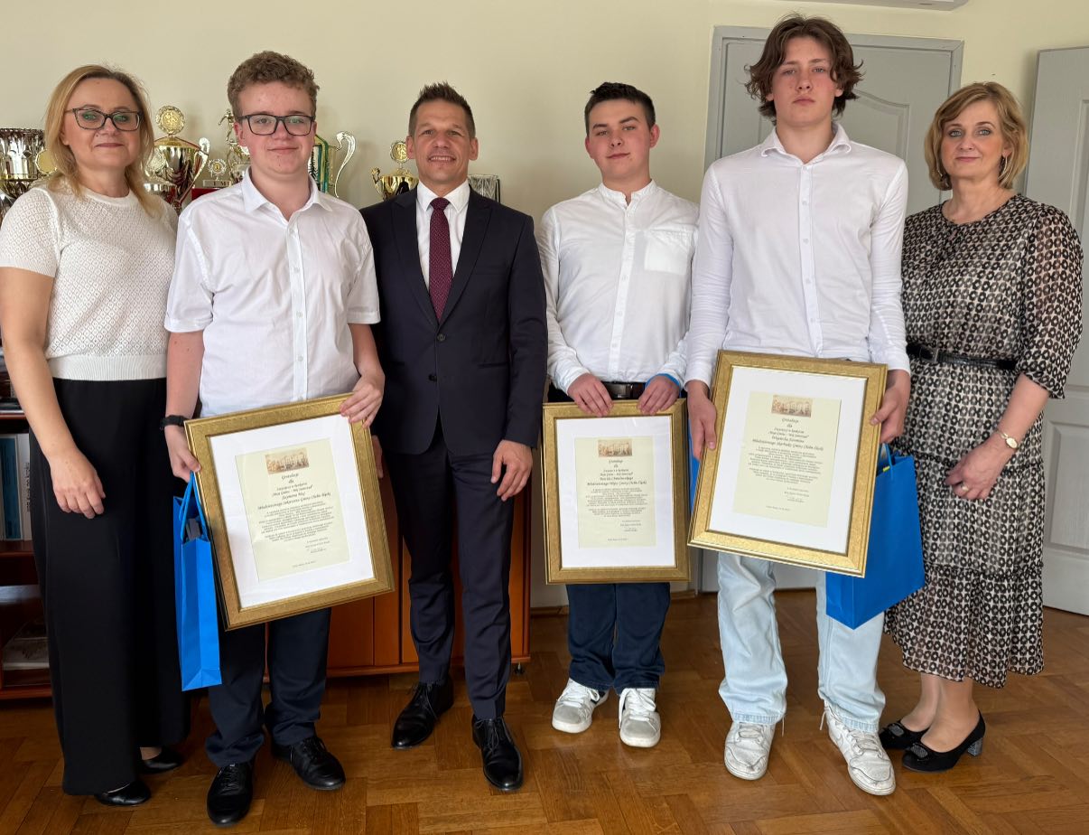 Osoby pozujące do zdjęcia z listami gratulacyjnymi w pomieszczeniu wójta 