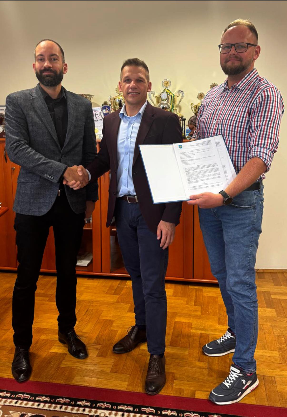 Trzej mężczyźni pozujący do zdjęcia z teczką podpisanych dokumetów