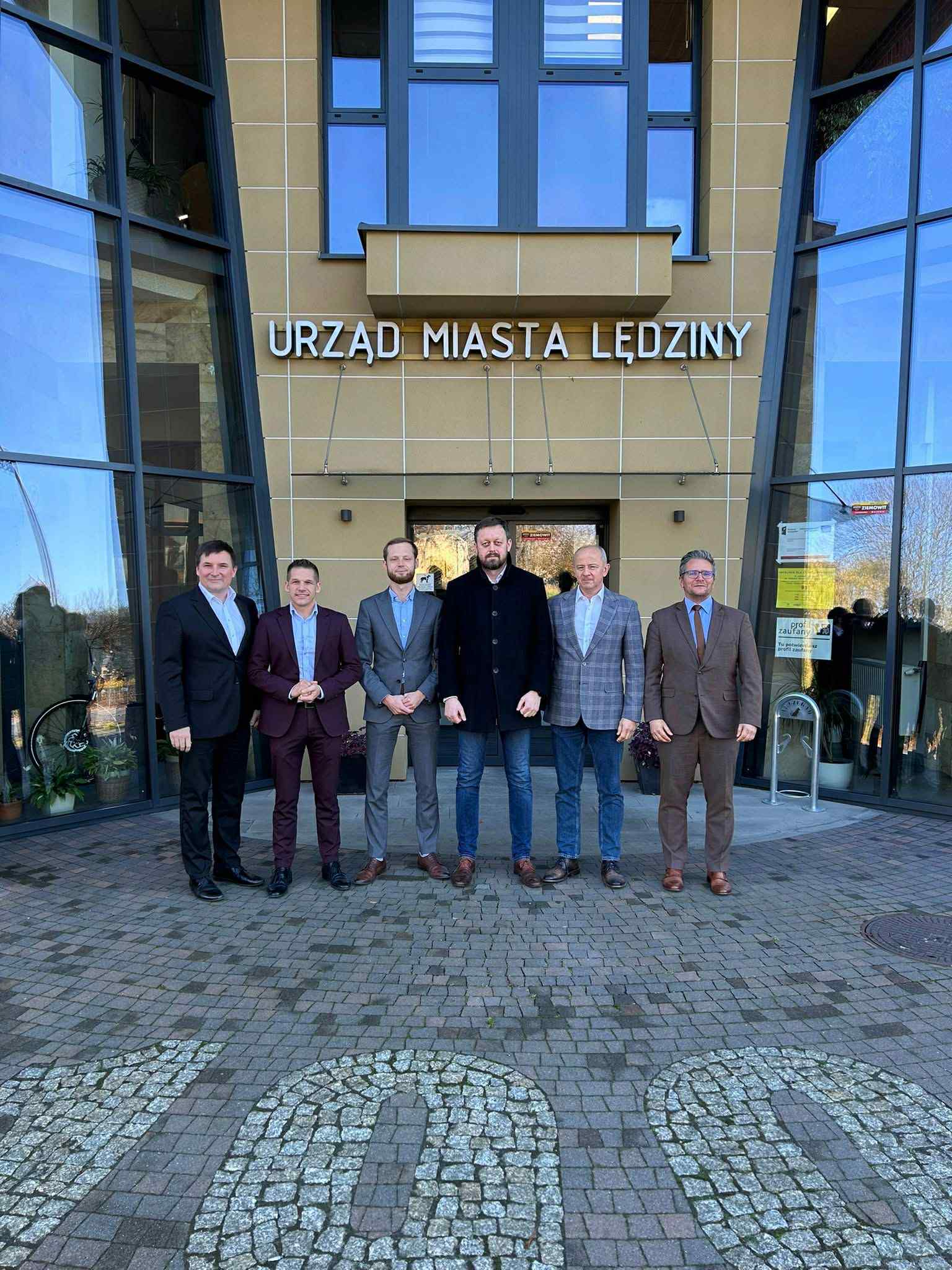 Sześciu mężczyzn pozujących przed budynkiem Urzędu Miasta 