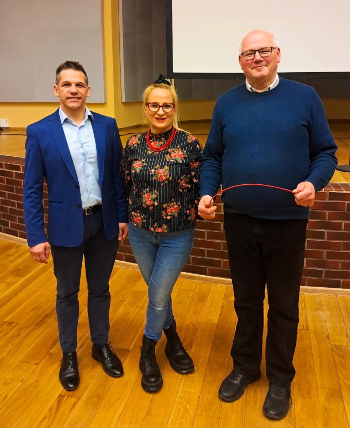 Trzy osoby pozujące w pomieszczeniu do zdjęcia. Dwaj mężczyźni i kobieta 