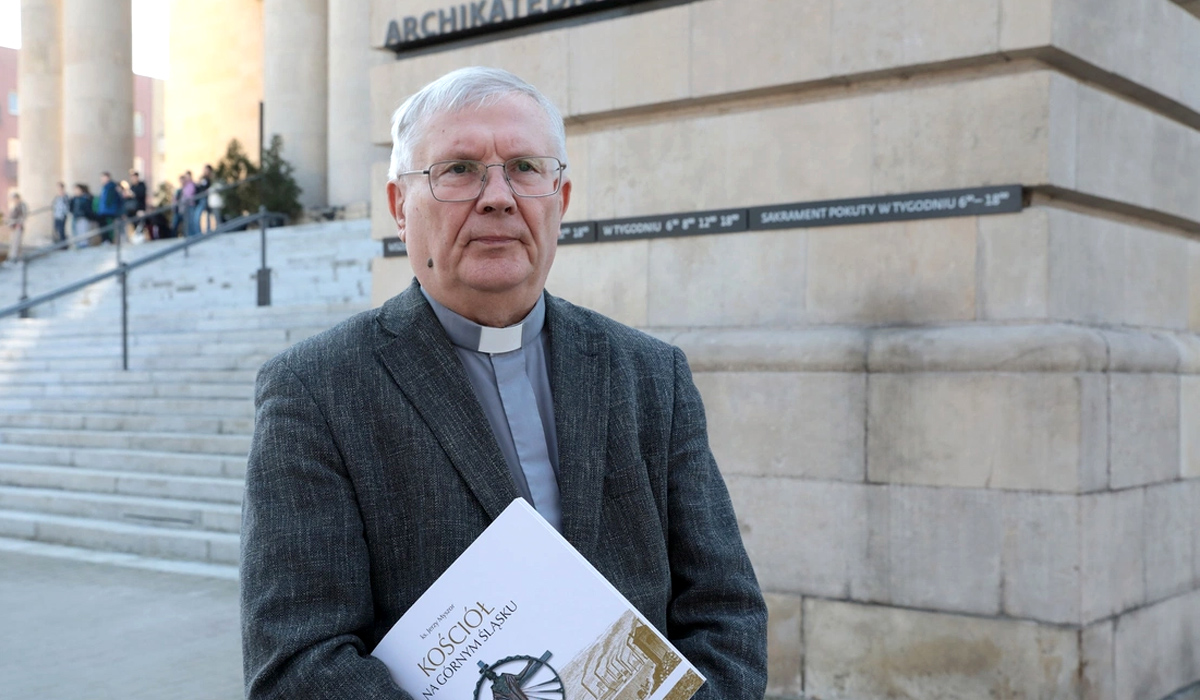 Mężczyzna - ksiądz stojący przed budynkiem 