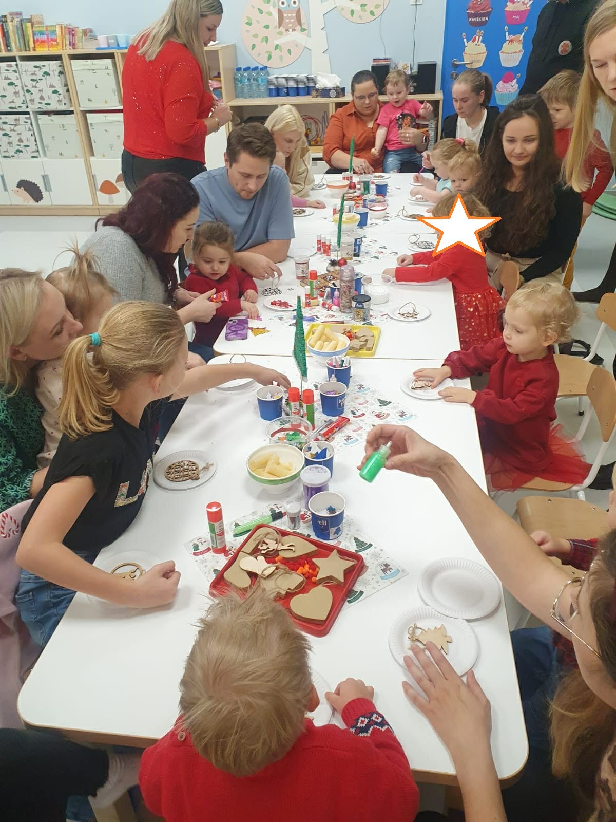 Rodzice i dzieci siedzące w sali za stolikiem - tworzą rękodzieło 