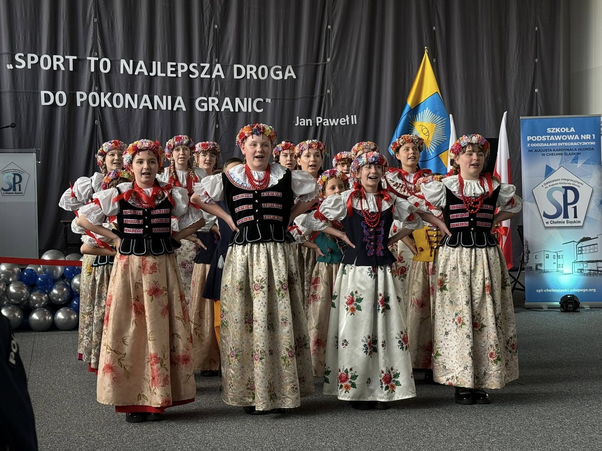 Dzieci w strojach ludowych śpiewające w pomieszczeniu 