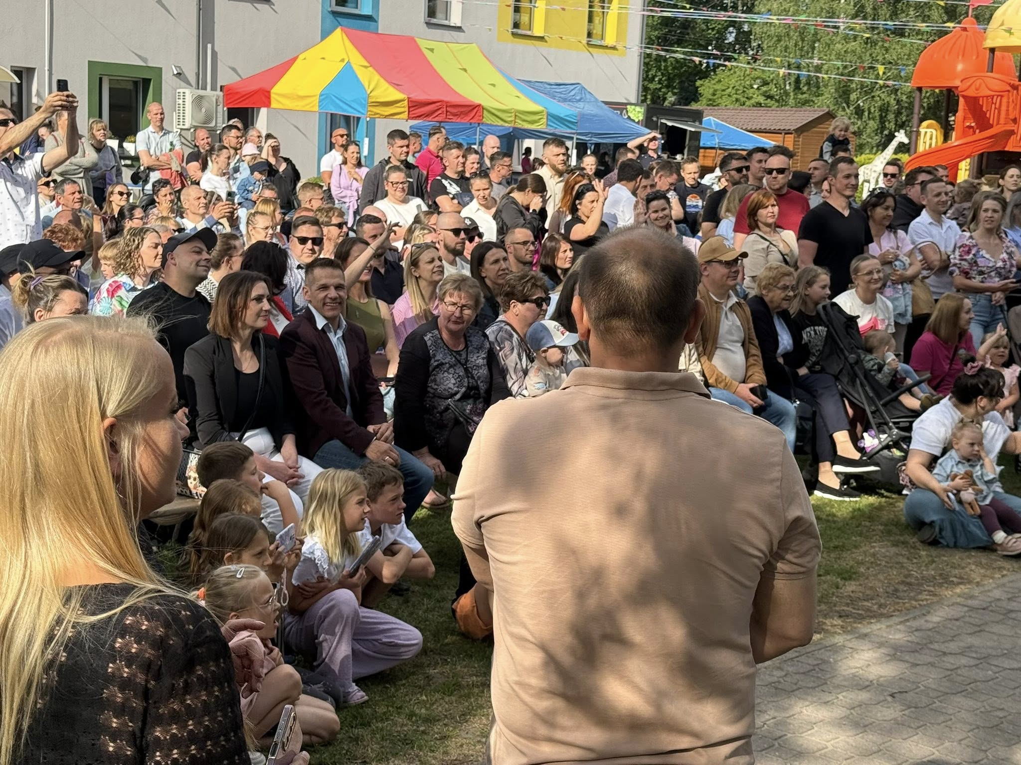 Rodzice siedzący na łąwkach i oglądający występy dzieci. 
