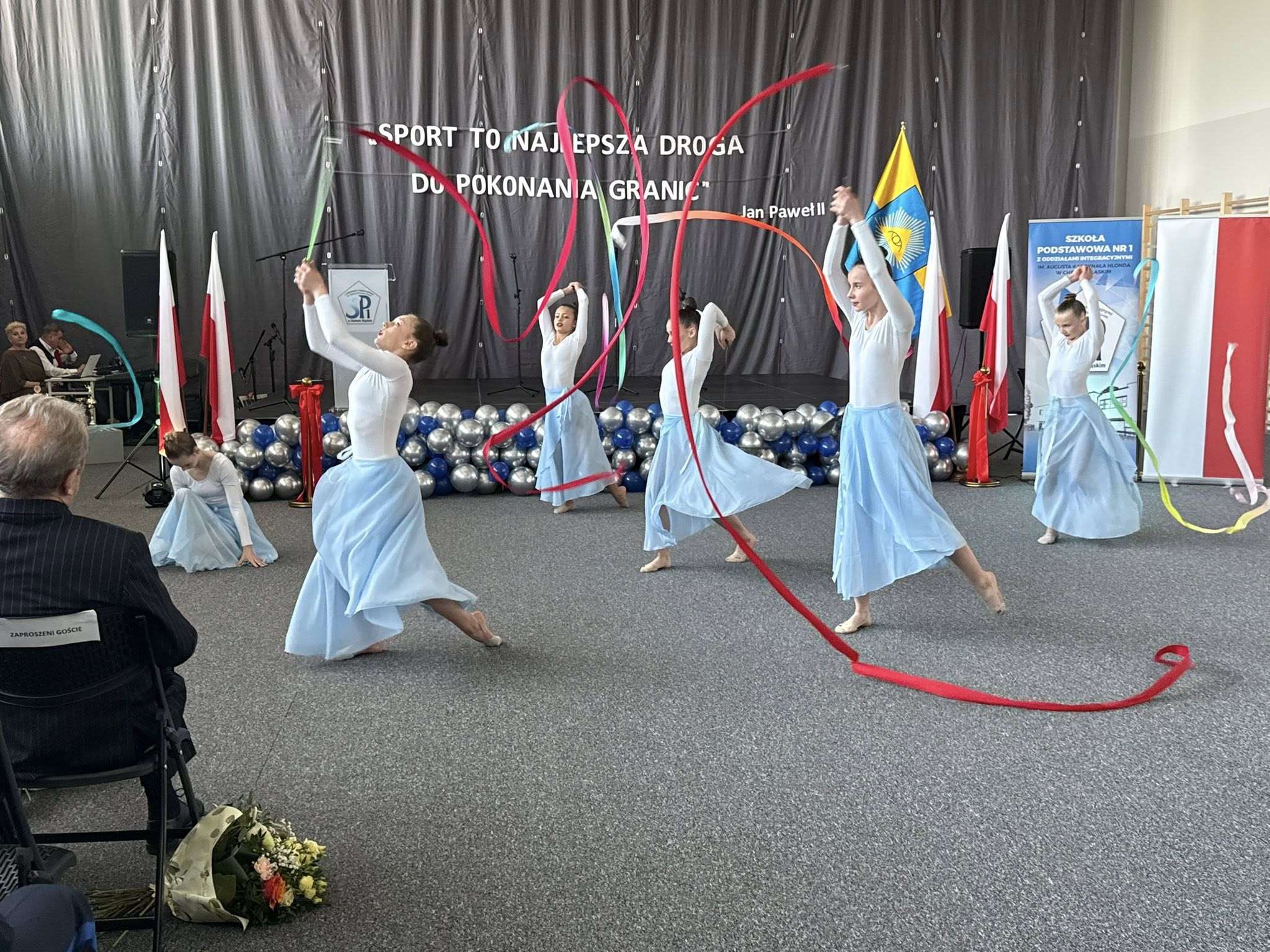 Młodzież w układzie tanecznymm z szarfami w pomieszczeniu 