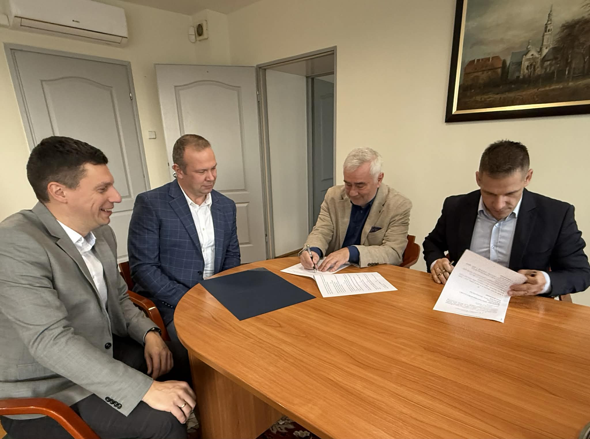 Czterech mężczyzn podpisujących porozumienie o wspłpracy siedzącycj za stołem w pomieszczeniu 