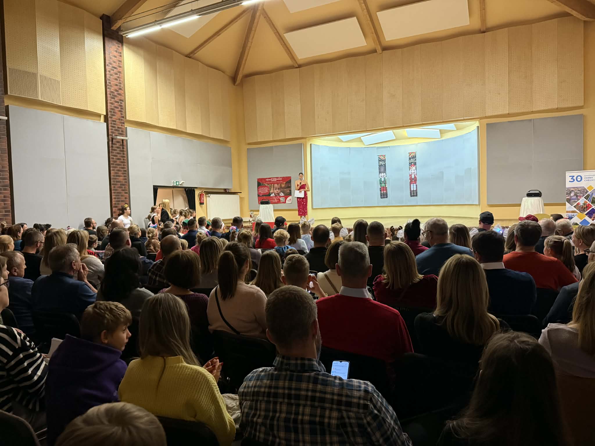 Ludzie siedzący w sali. Kobieta przemawia ze sceny 