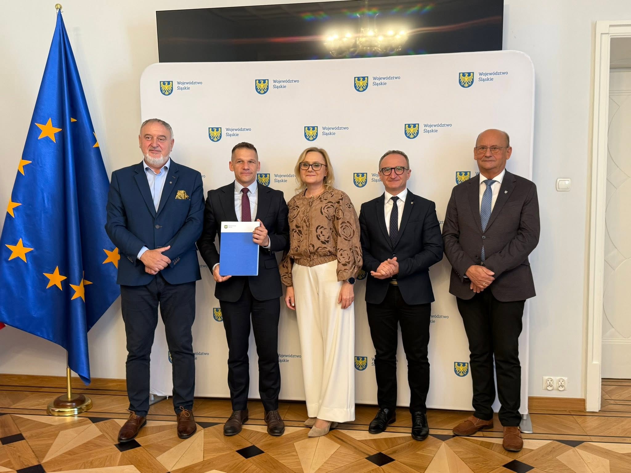 Pięć osób pozujacych do zdjecia w pomieszczeniu na ściance reklamowej 
