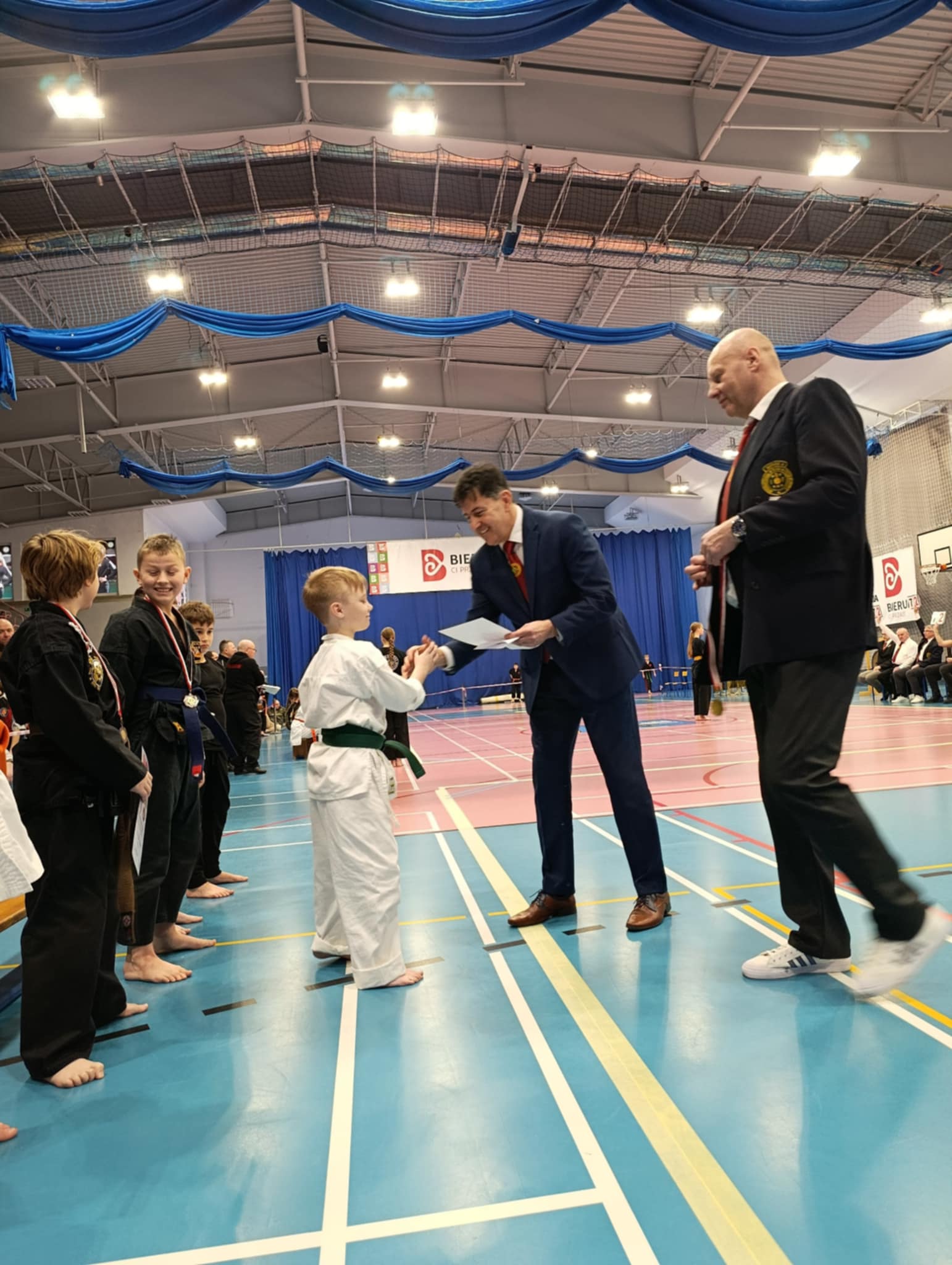 Rozdanie medali w hali sportowej. Na zdjęciu zawodnicy i trenerzy