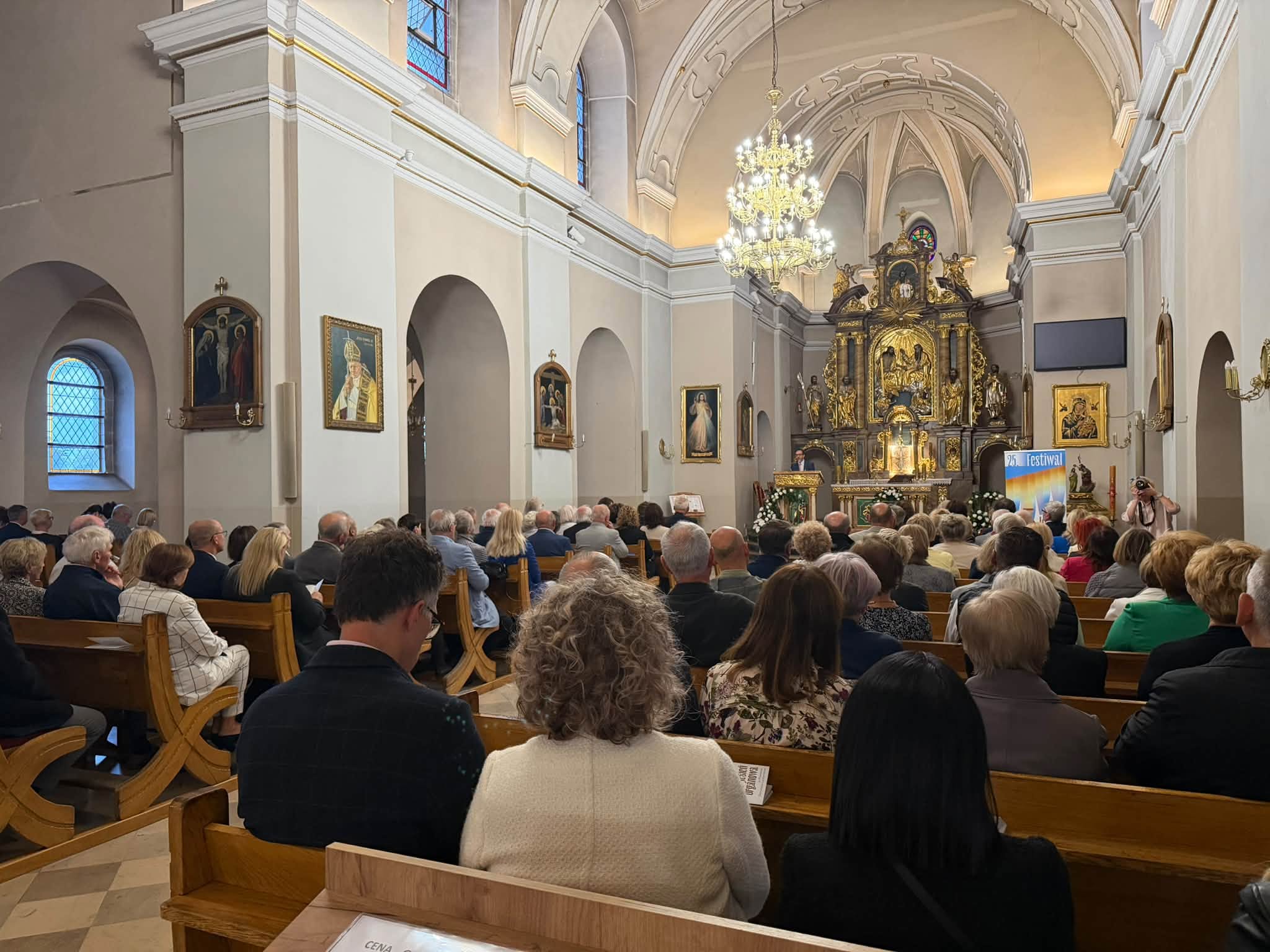 Wnętrze kościoła ze zgromadzonymi wiernymi, siedzącymi w ławkach 