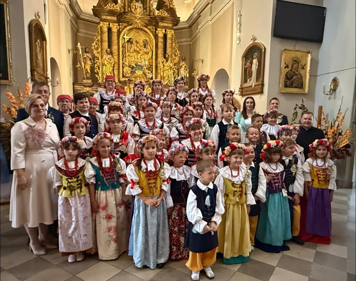 Dzieci w strojach ludowych i dorośli pozujacy do zdjęcia przed ołtarzem w kościele 
