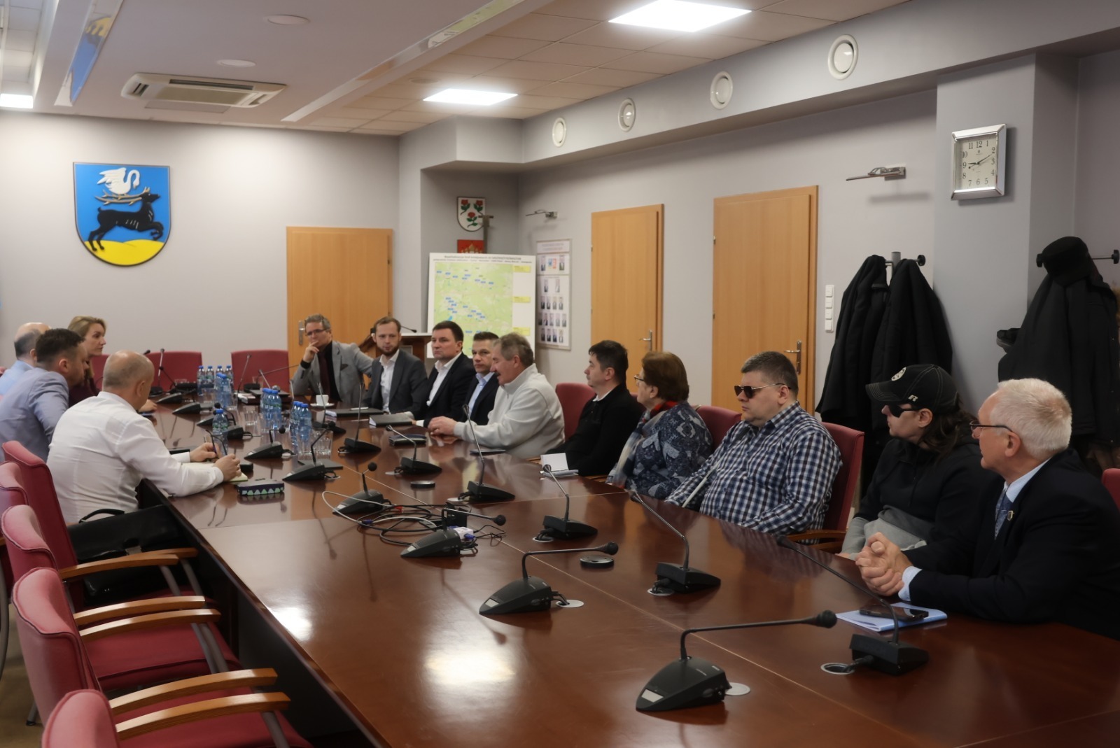 Osoby siedzące za stołem konferencyjnym w pomieszczeniu. Prowadzone są rozmowy 