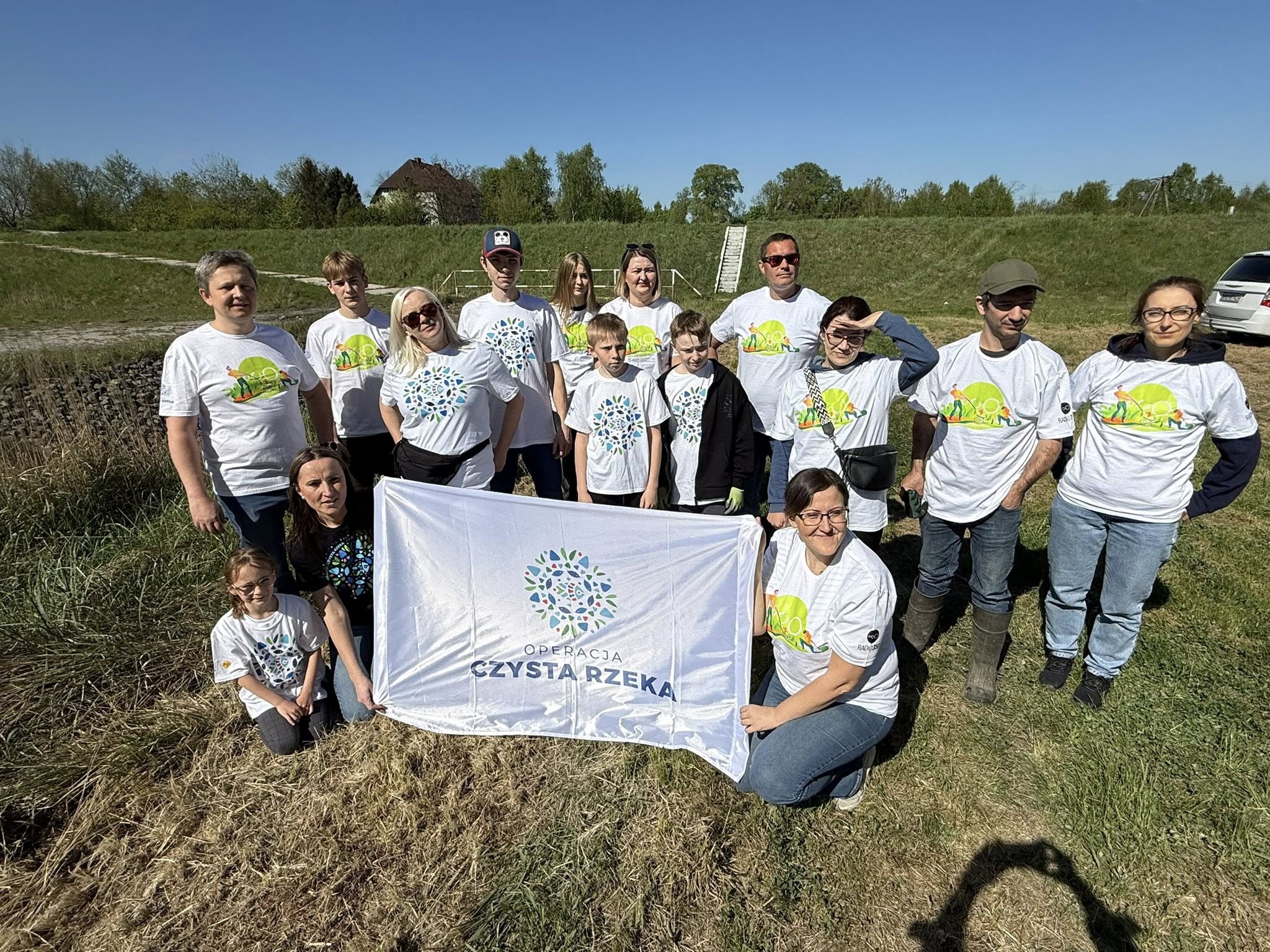 Osoby na łące z banerem Czyta rzeka 