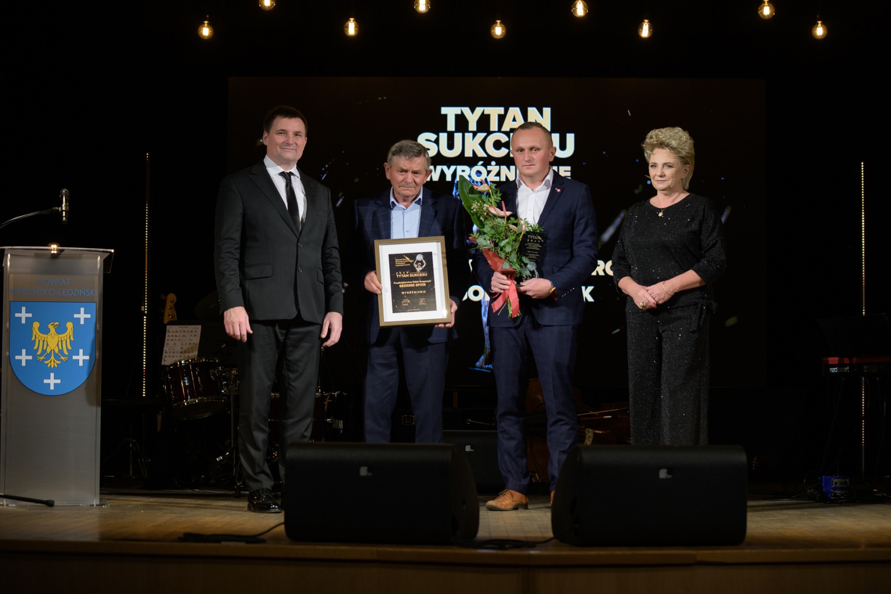 Trzech mężczyzn i kobieta stojący na scenie z podziękowaniami - pozujący do zdjęcia 