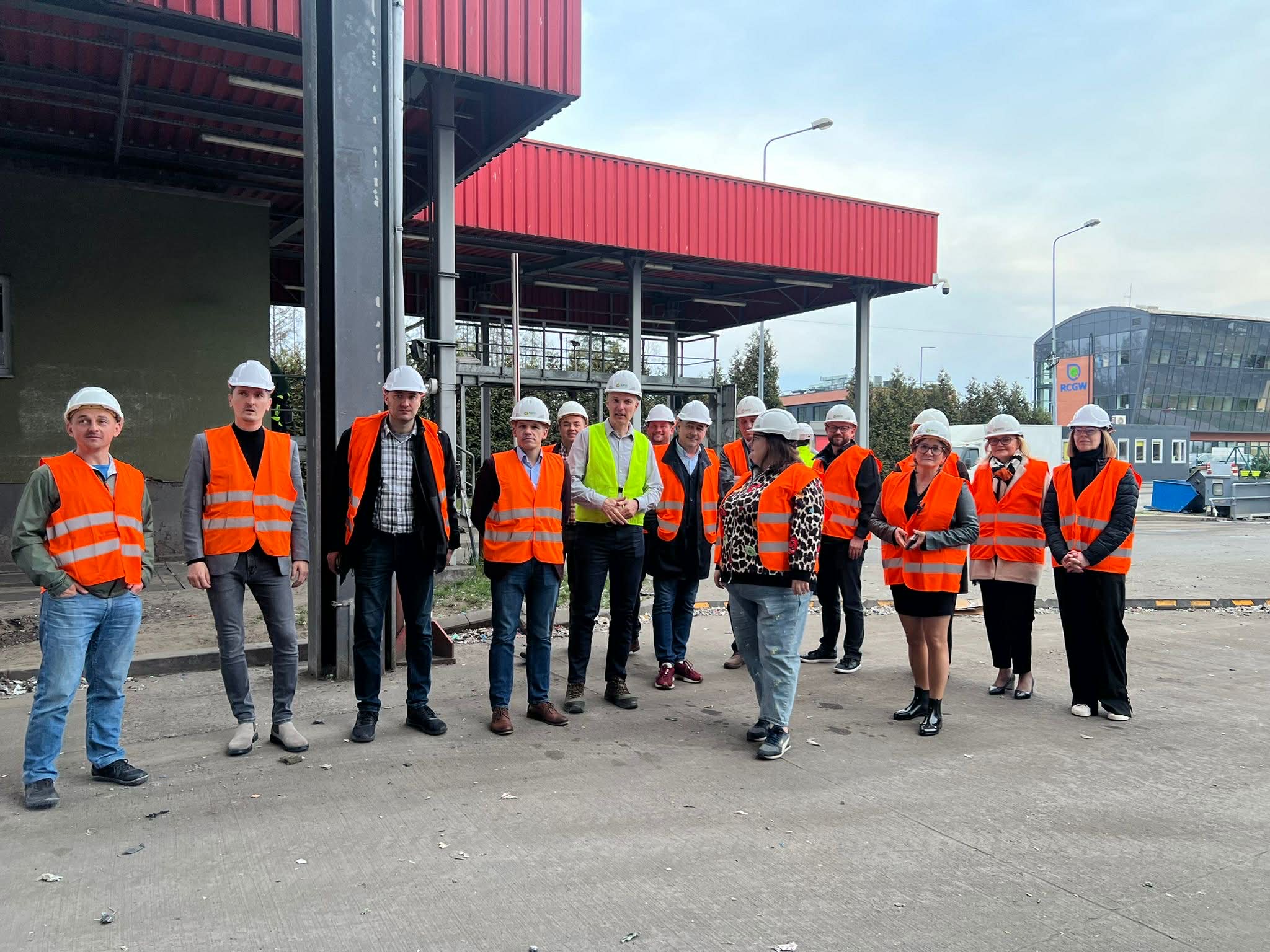 Osoby pozujące do zdjęcia w kamizelkach odblaskowych i kaskach przed budynkiem 