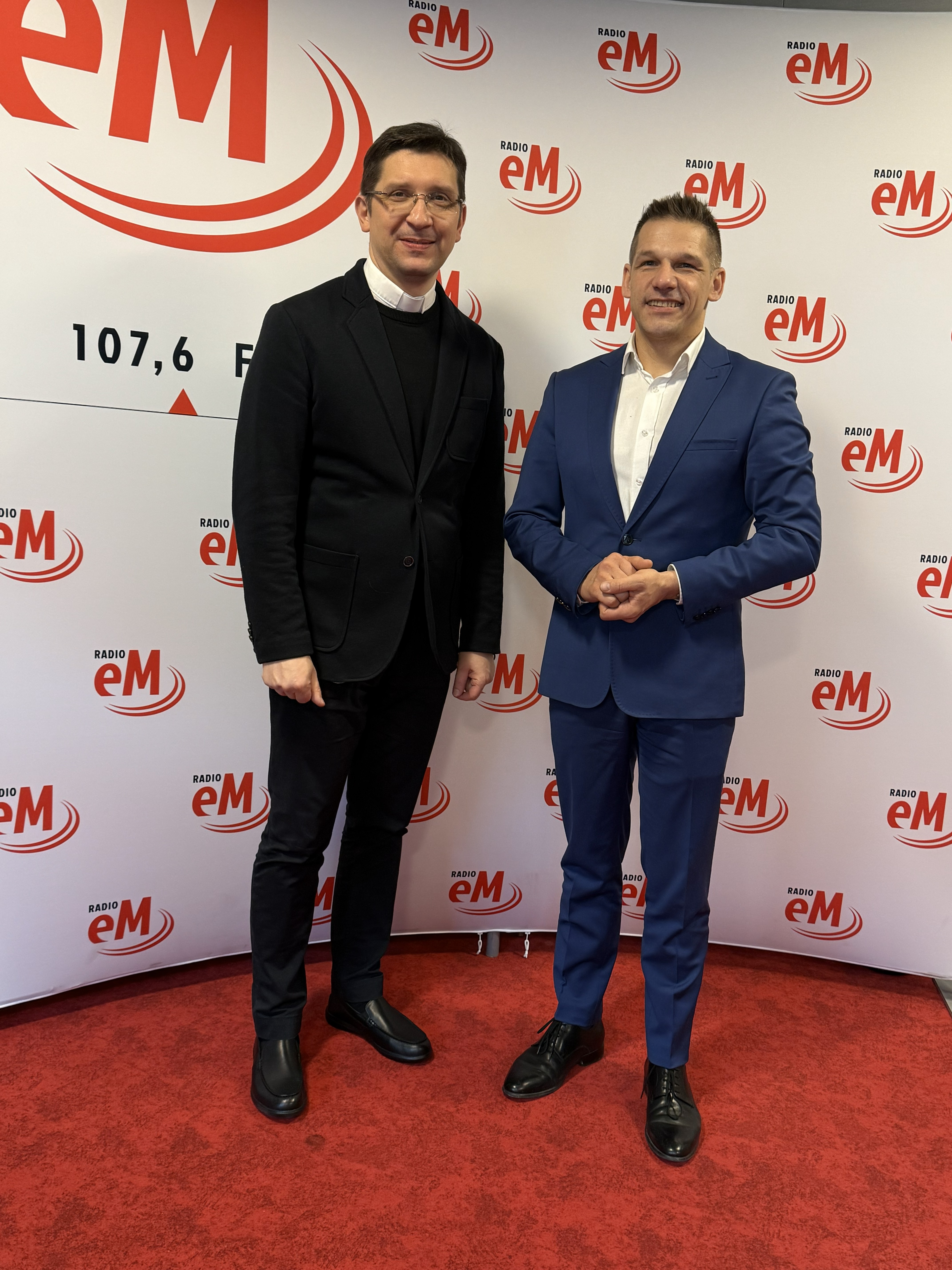Dwaj mężczyźni pozujacy do zdjęcia przed ścianką promocyjną radia eM