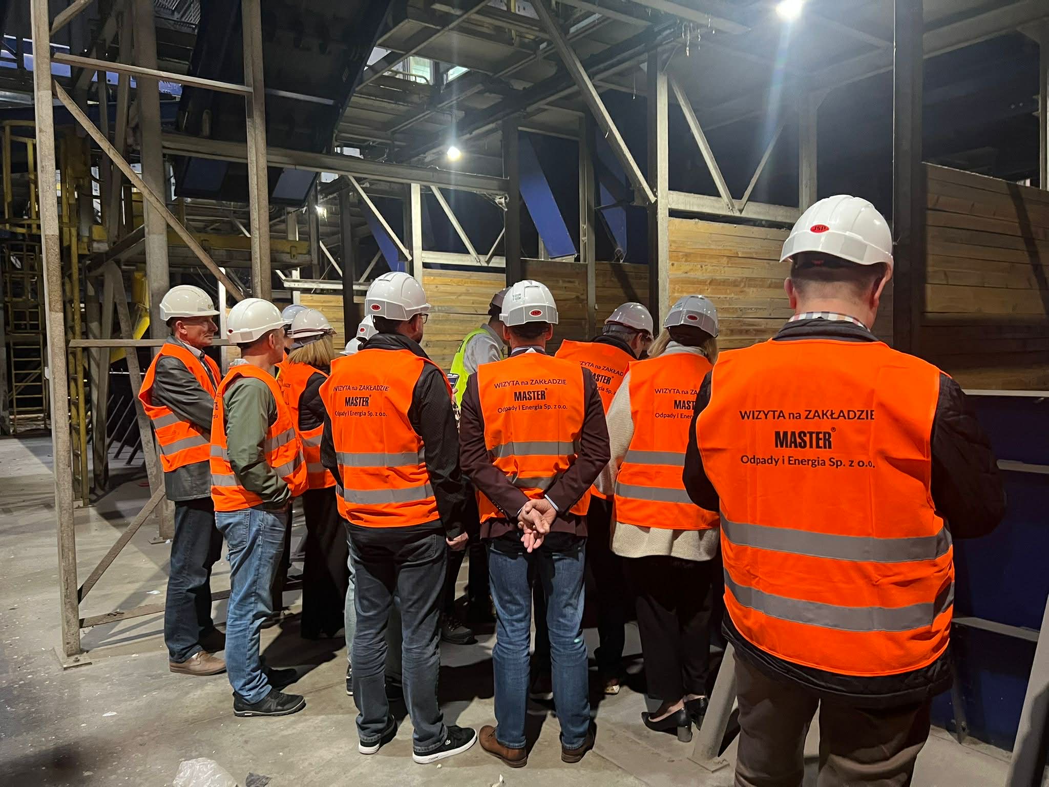 Osoby stojące w pomieszczeniu w kamizelkach odblaskowych i kaskach 