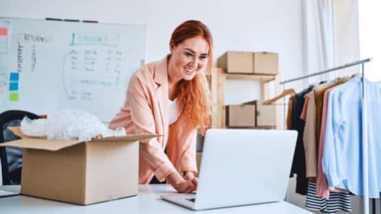 Kobieta znajdująca się przy komputerze i kartonach w pomieszczeniu 