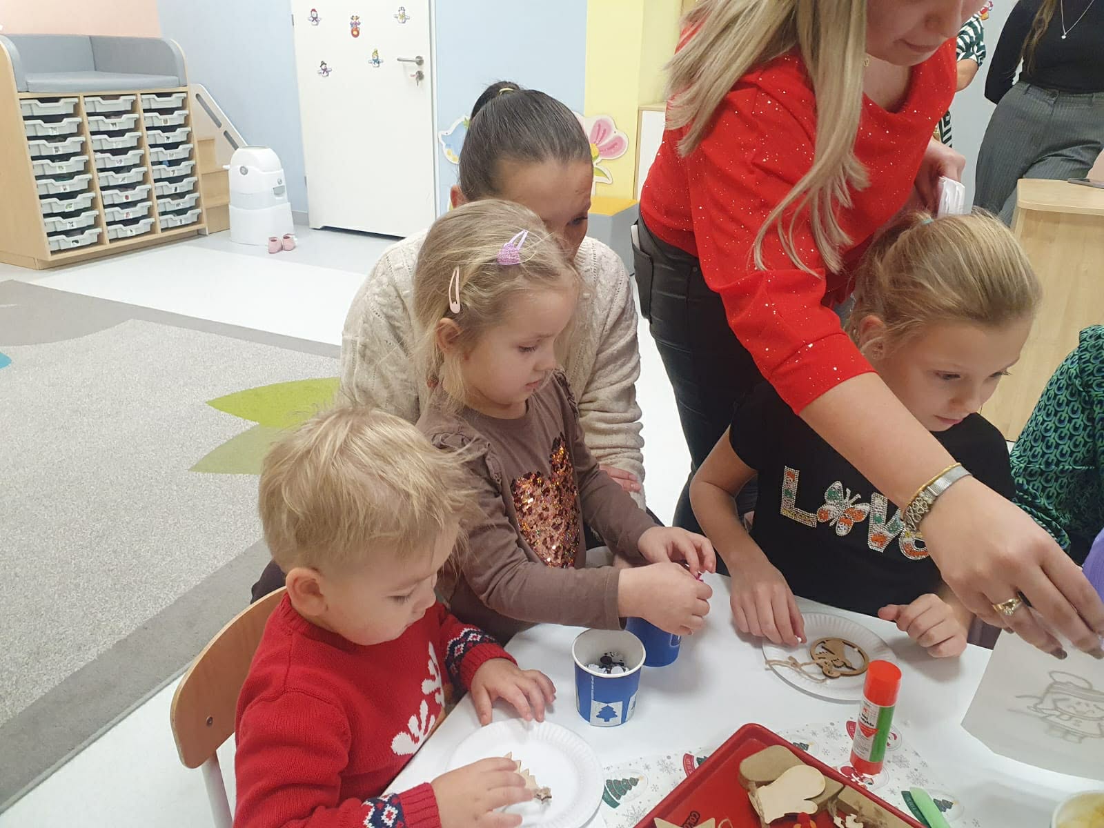 Rodzice i dzieci siedzące w sali za stolikiem - tworzą rękodzieło 