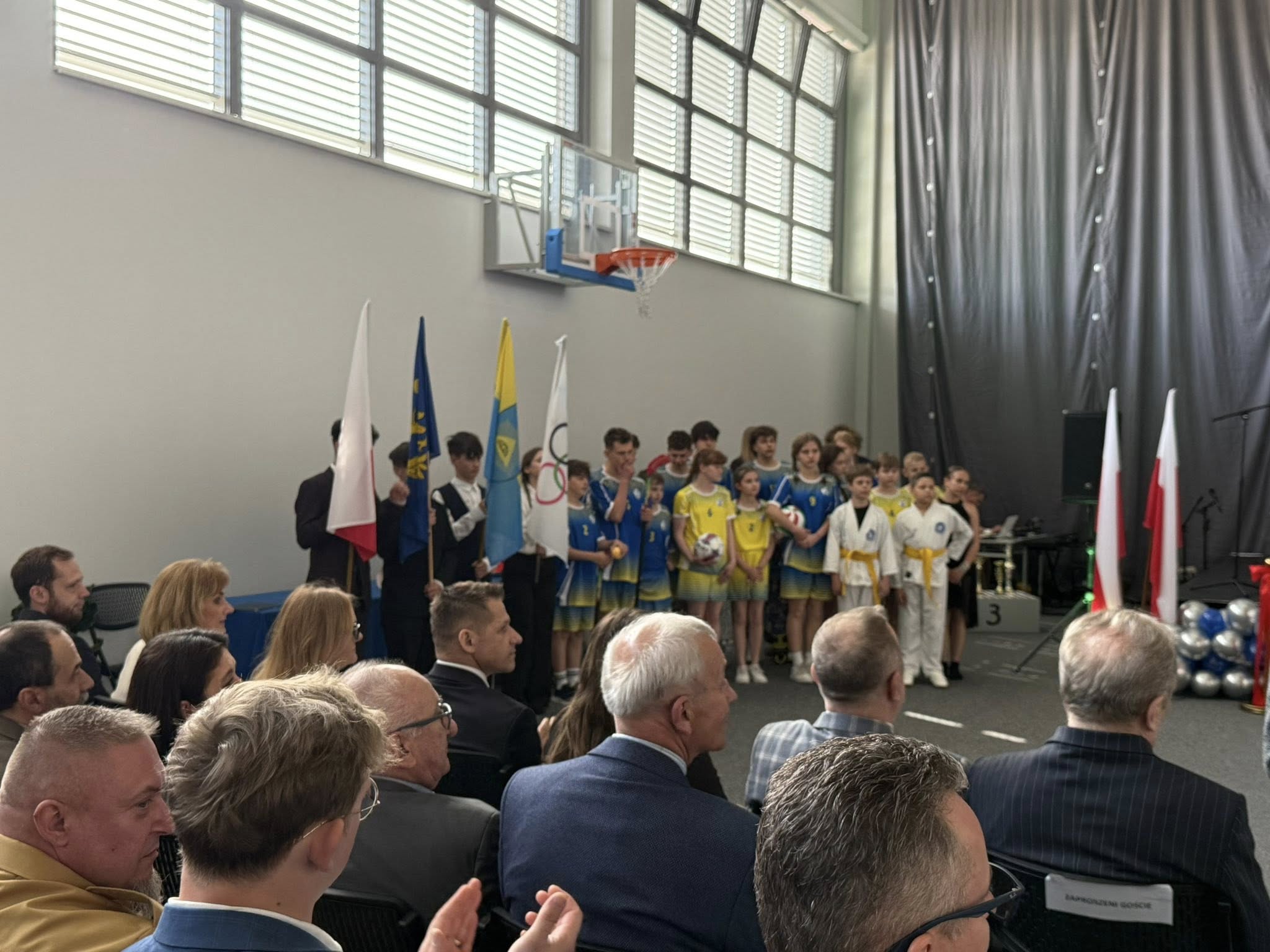 Uczestnicy uroczystości w pomieszczeniu. Dzieci w strojach sportowych 