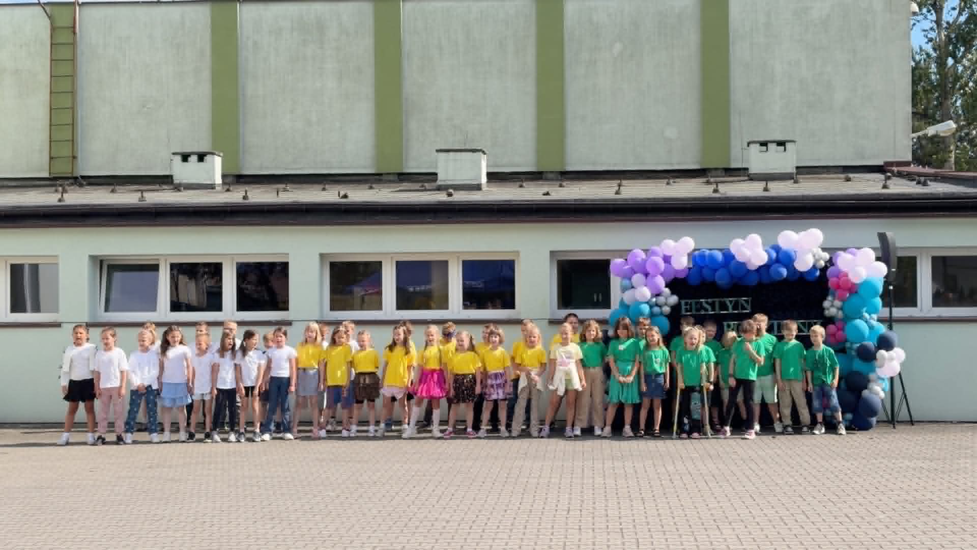 Dzieci stojące na boisku przed budynkiem szkoły. Prezentowały one częśc artystyczną. 