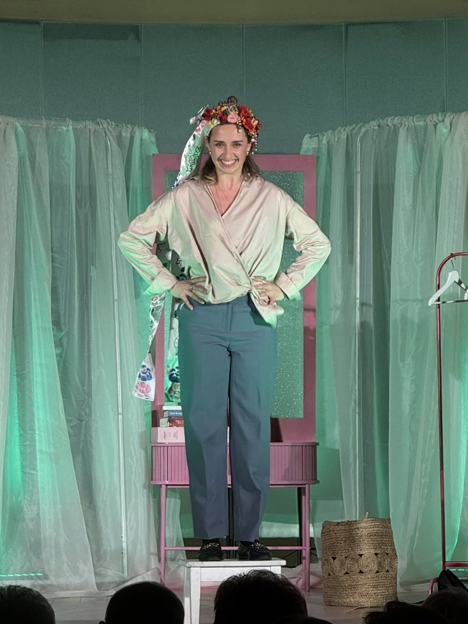 Uśmiechnięta dziewczyna w wianku na głowie, stojąca na krzesełku na scenie. 